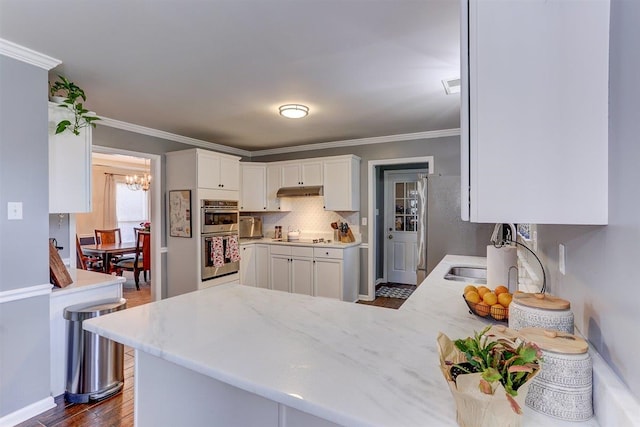 8973 E Carrollwood Ln, Memphis, TN 38016 - kitchen with stainless steel appliances, a chandelier, white cabinets, dark wood-type flooring, and light stone counters