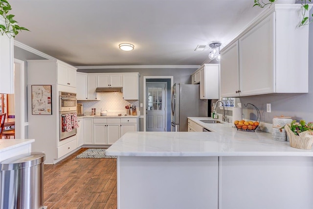 8973 E Carrollwood Ln, Memphis, TN 38016 - kitchen featuring appliances with stainless steel finishes, under cabinet range hood, a peninsula, white cabinetry, and wood finished floors