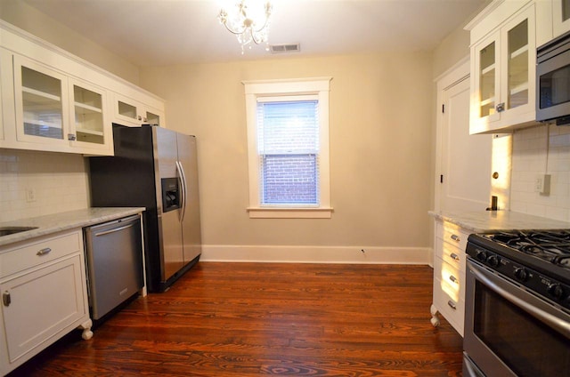 kitchen with dark hardwood / wood-style flooring, white cabinetry, appliances with stainless steel finishes, backsplash, and light stone counters