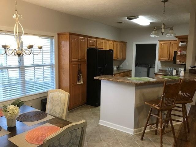 kitchen featuring light tile flooring, a chandelier, black fridge, independent washer and dryer, and pendant lighting