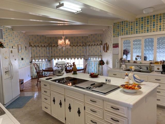 kitchen with an inviting chandelier, beamed ceiling, tile countertops, white cabinetry, and white fridge with ice dispenser