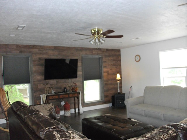 living room with ceiling fan, a wood stove, wooden walls, and a textured ceiling