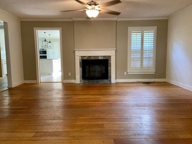 unfurnished living room with a premium fireplace, crown molding, hardwood / wood-style floors, a textured ceiling, and ceiling fan with notable chandelier