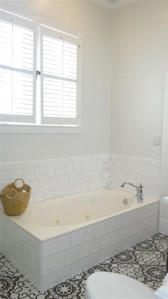 bathroom featuring toilet, tile flooring, plenty of natural light, and a relaxing tiled bath