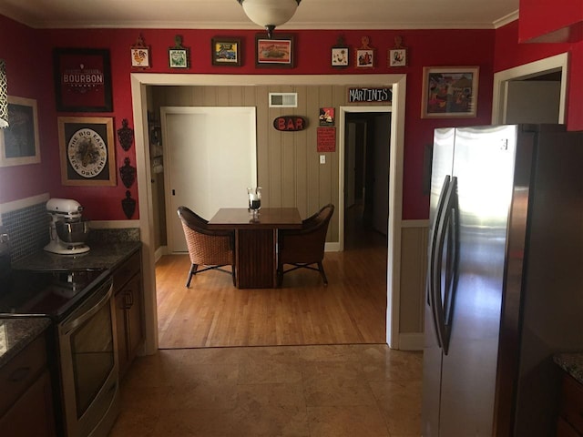 kitchen featuring dark stone counters, ornamental molding, appliances with stainless steel finishes, and light hardwood / wood-style floors