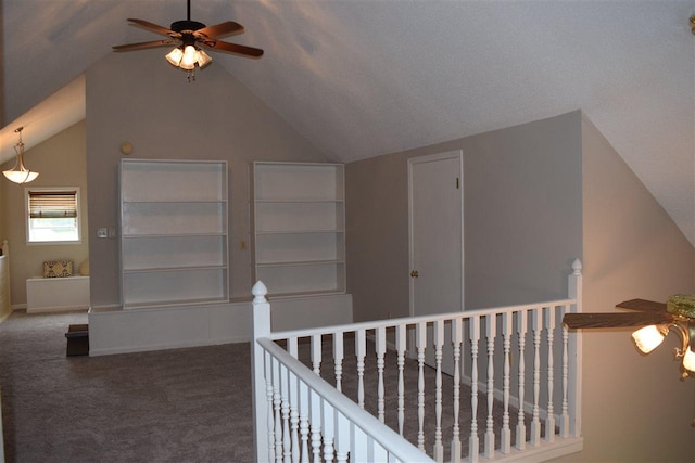 hallway featuring a textured ceiling, vaulted ceiling, and dark colored carpet