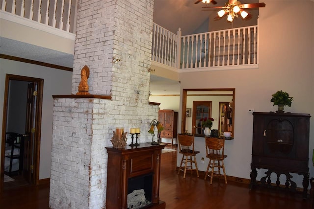 living room with dark wood-type flooring, ceiling fan, a towering ceiling, brick wall, and ornamental molding