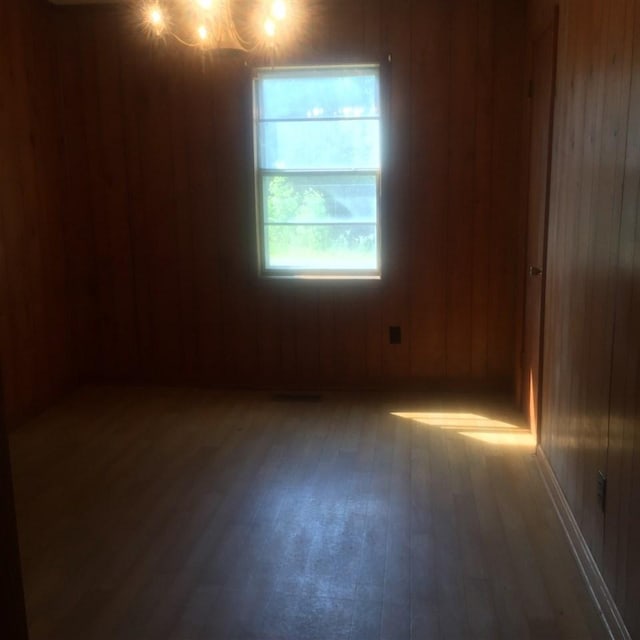 spare room with an inviting chandelier, wooden walls, and dark hardwood / wood-style floors