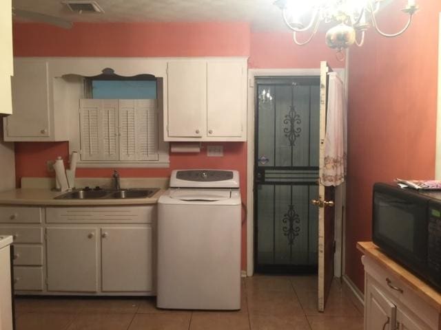 kitchen with sink, light tile floors, washer / dryer, an inviting chandelier, and white cabinetry