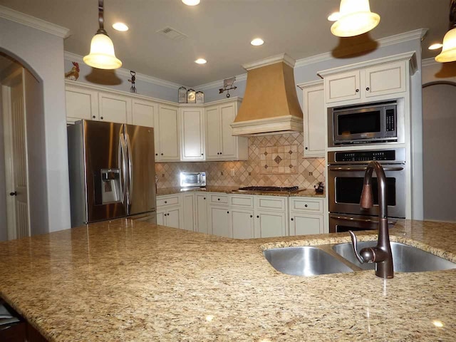 kitchen with light stone counters, stainless steel appliances, custom exhaust hood, pendant lighting, and backsplash