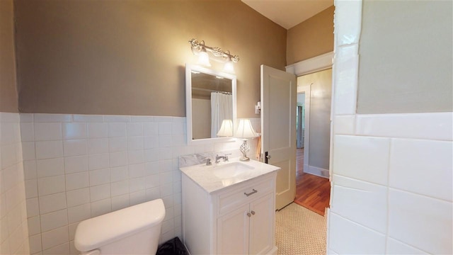 bathroom with tile walls, vanity with extensive cabinet space, toilet, and hardwood / wood-style flooring