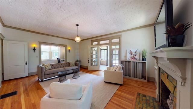 living room featuring ornamental molding, light hardwood / wood-style flooring, a textured ceiling, and a tiled fireplace