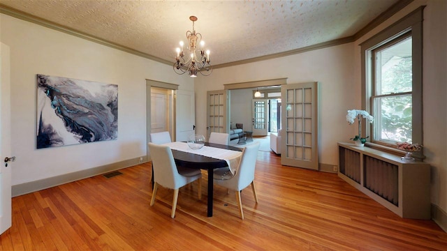 dining space featuring french doors, crown molding, a textured ceiling, a notable chandelier, and light wood-type flooring