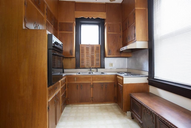 kitchen with gas stovetop, black oven, light tile floors, and sink