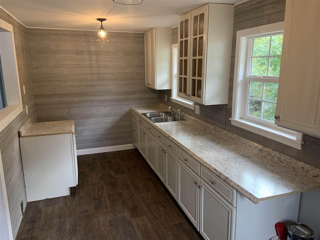 kitchen with sink, wood walls, dark wood-type flooring, decorative light fixtures, and white cabinetry