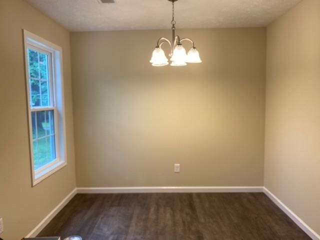 spare room with dark hardwood / wood-style flooring and an inviting chandelier