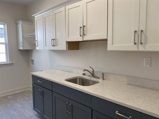 kitchen with white cabinets, light stone counters, sink, and light hardwood / wood-style flooring