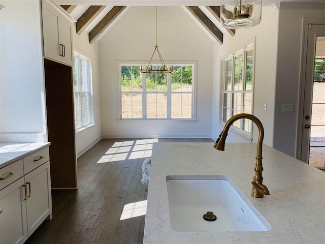 kitchen with pendant lighting, beam ceiling, dark wood-type flooring, sink, and light stone counters