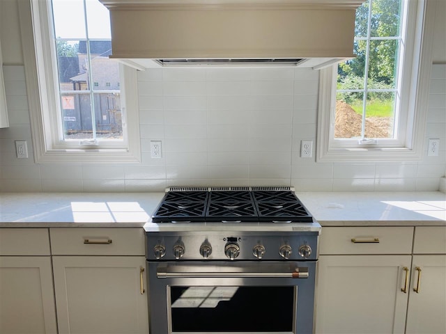 kitchen with backsplash, light stone counters, high end range, and plenty of natural light