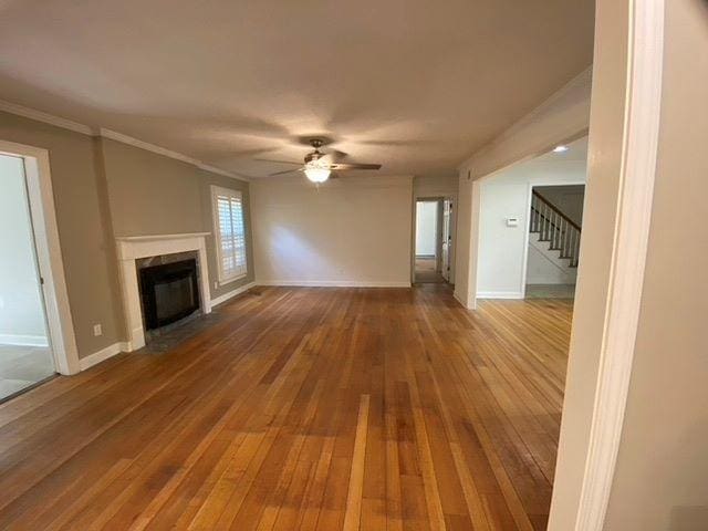 unfurnished living room with ornamental molding, ceiling fan, and dark wood-type flooring