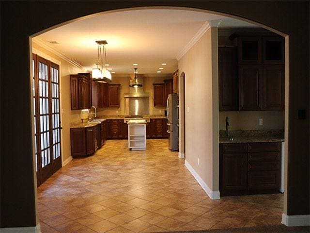 kitchen with light tile flooring, hanging light fixtures, a center island, stainless steel fridge, and crown molding