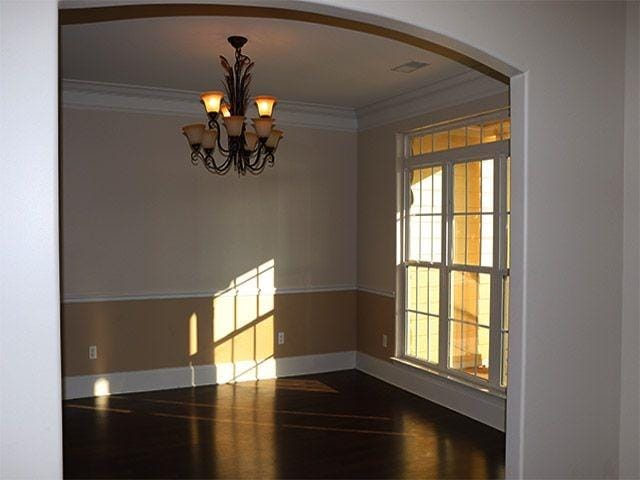 unfurnished room with a wealth of natural light, crown molding, dark hardwood / wood-style floors, and an inviting chandelier