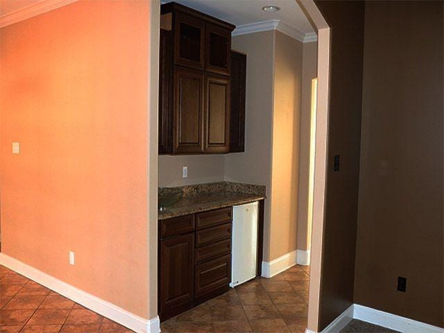 kitchen featuring light stone countertops, dark tile flooring, dark brown cabinets, and ornamental molding