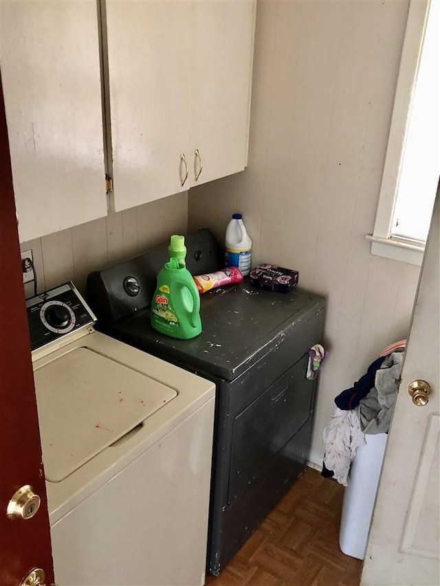 washroom with dark parquet flooring, washing machine and dryer, and cabinets