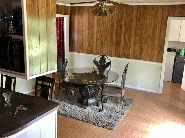 dining area with wood walls, washer / clothes dryer, ceiling fan, and light parquet floors