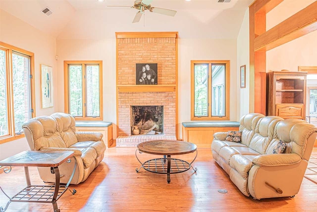 living room featuring ceiling fan, brick wall, high vaulted ceiling, a brick fireplace, and light wood-type flooring