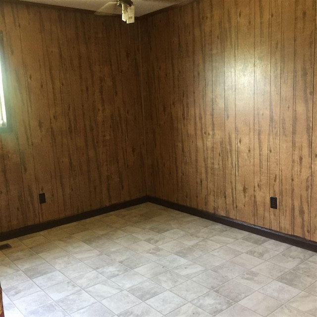 tiled empty room featuring ceiling fan and wood walls