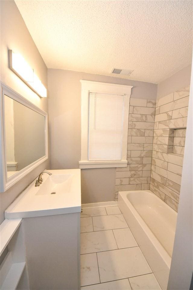 bathroom with tiled shower / bath combo, a textured ceiling, tile flooring, and vanity with extensive cabinet space