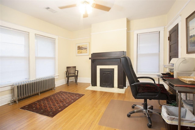 home office featuring light hardwood / wood-style floors, ceiling fan, and radiator heating unit