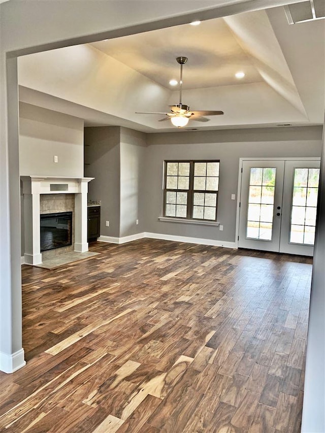 unfurnished living room with dark hardwood / wood-style flooring, ceiling fan, a tray ceiling, and french doors