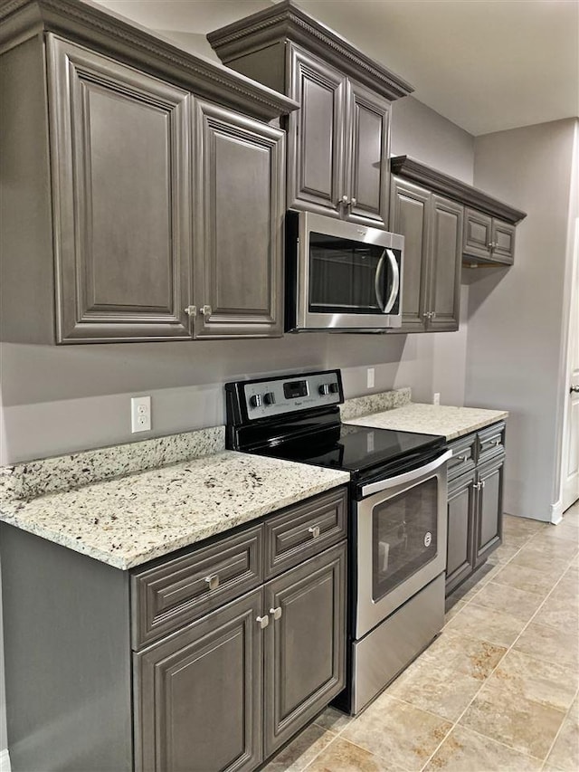 kitchen featuring light tile floors, dark brown cabinets, light stone counters, and stainless steel appliances