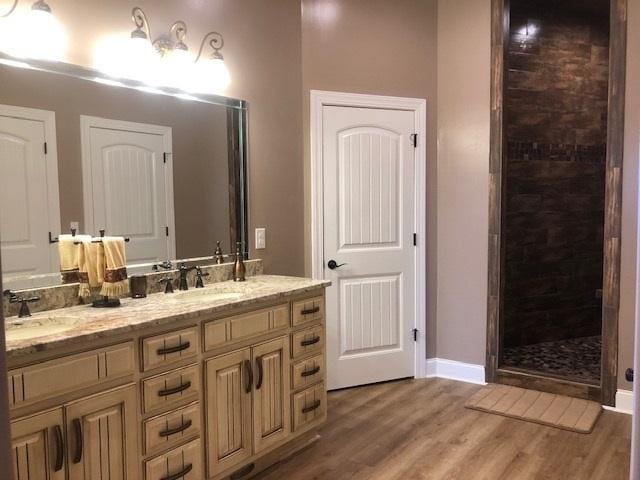 bathroom featuring dual vanity, wood-type flooring, and tiled shower