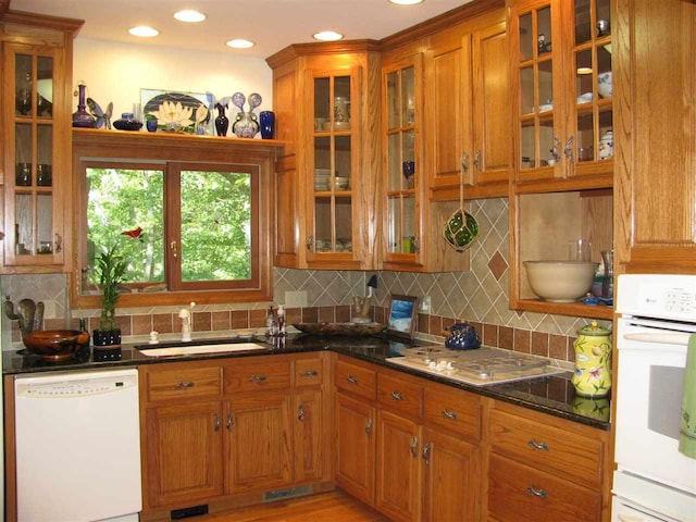 kitchen with dark stone counters, tasteful backsplash, white appliances, and sink