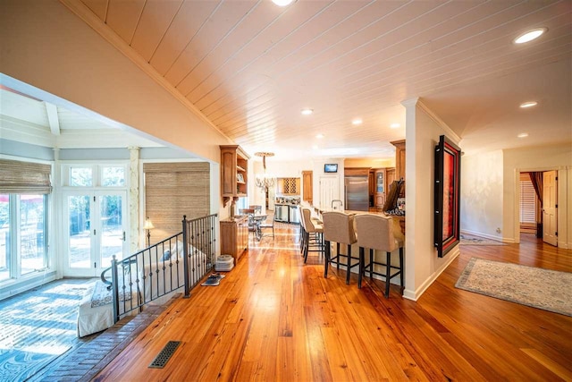 hallway with ornate columns, beamed ceiling, french doors, wood-type flooring, and ornamental molding