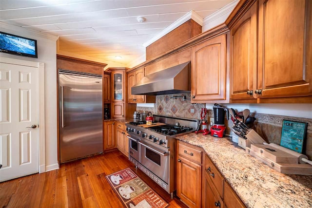 kitchen with high quality appliances, light hardwood / wood-style floors, wall chimney range hood, light stone countertops, and backsplash