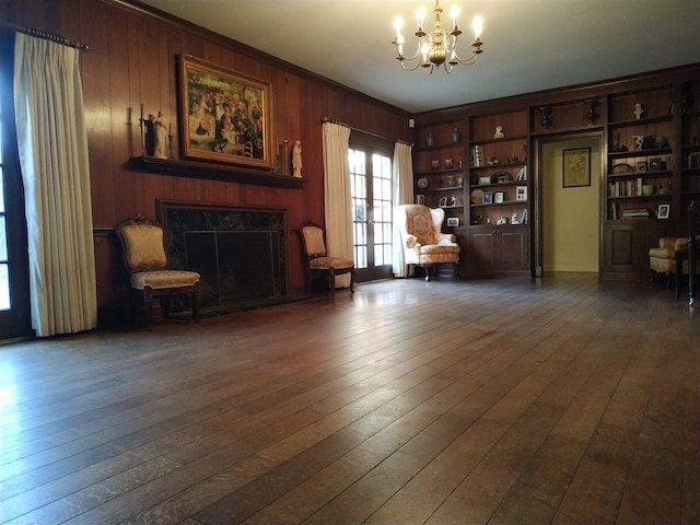 living room featuring an inviting chandelier, a high end fireplace, wood walls, dark hardwood / wood-style flooring, and built in shelves