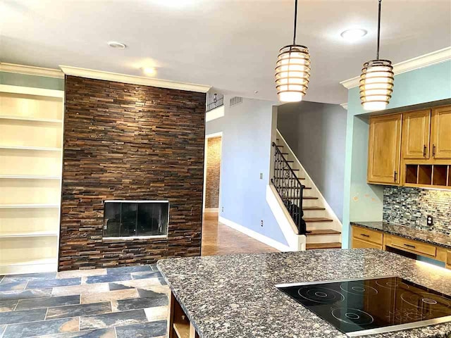 kitchen with hanging light fixtures, backsplash, a stone fireplace, dark stone counters, and black electric stovetop