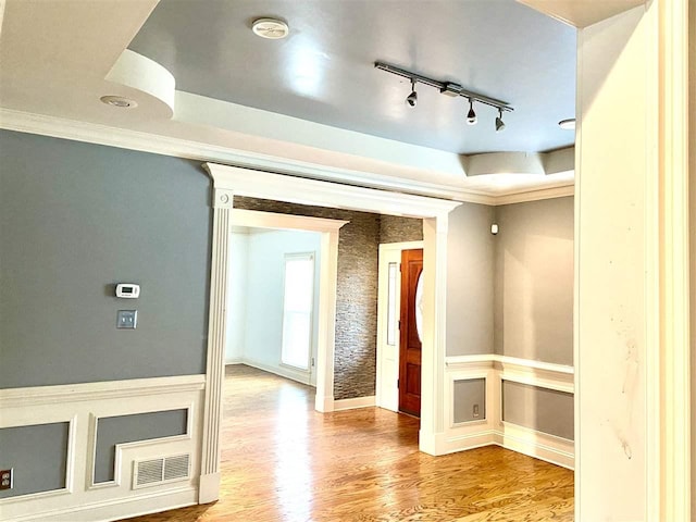 interior space with a tray ceiling, ornamental molding, light hardwood / wood-style floors, and track lighting