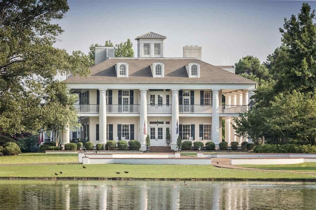 rear view of house with a balcony, a lawn, french doors, and a water view