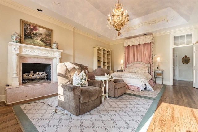 bedroom featuring an inviting chandelier, light wood-type flooring, a premium fireplace, a raised ceiling, and ornamental molding