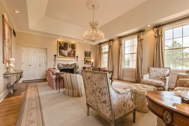 living area with a notable chandelier, a healthy amount of sunlight, light hardwood / wood-style floors, and a raised ceiling