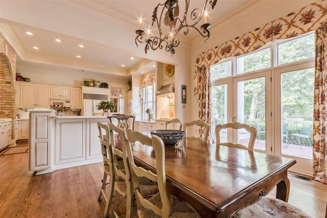 dining space featuring ornamental molding, a raised ceiling, a chandelier, and light hardwood / wood-style floors