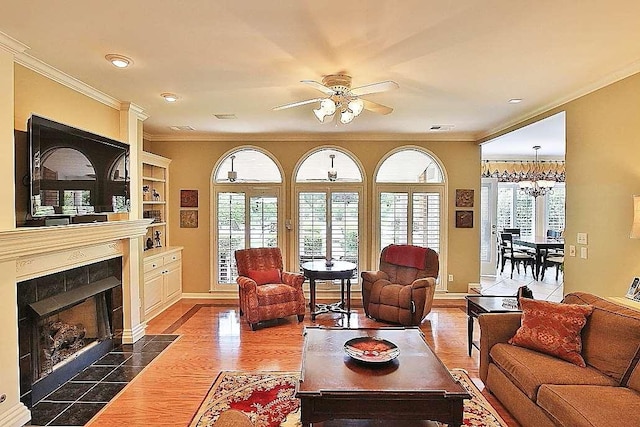 living room with a tiled fireplace, dark hardwood / wood-style floors, ceiling fan with notable chandelier, ornamental molding, and built in shelves