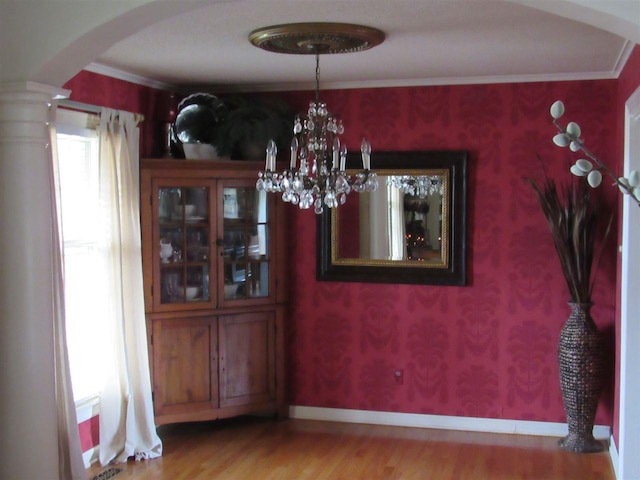 unfurnished dining area with light hardwood / wood-style flooring, a notable chandelier, and ornate columns