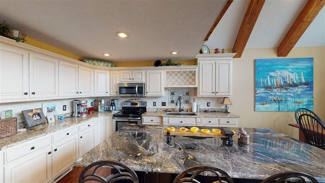 kitchen with a kitchen island, appliances with stainless steel finishes, beamed ceiling, and dark stone countertops