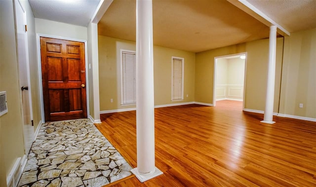 foyer entrance featuring a textured ceiling, ornate columns, and light wood-type flooring